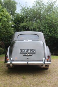 Rolls royce silver dawn rally car, rear view. Car is silver/grey with rally stickers on the side