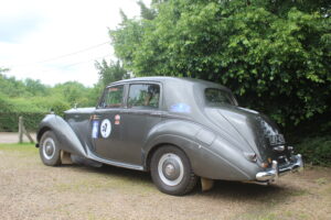 Rolls royce silver dawn rally car, 3/4 profile. Car is silver/grey with rally stickers on the side