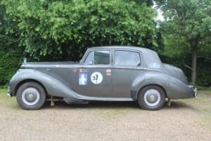 Rolls royce silver dawn rally car, passenger's side profile. Car is silver/grey with rally stickers on the side