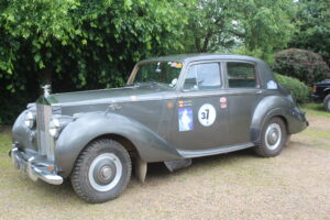 Rolls royce silver dawn rally car, 3/4 profile. Car is silver/grey with rally stickers on the side