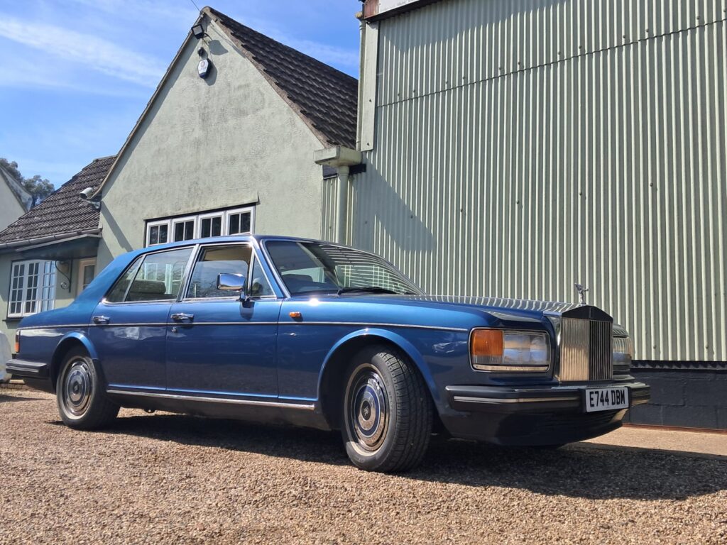 Rolls-Royce silver spirit front three quarters view, in mid blue. Harvey Wash workshop is behind the vehicle. 